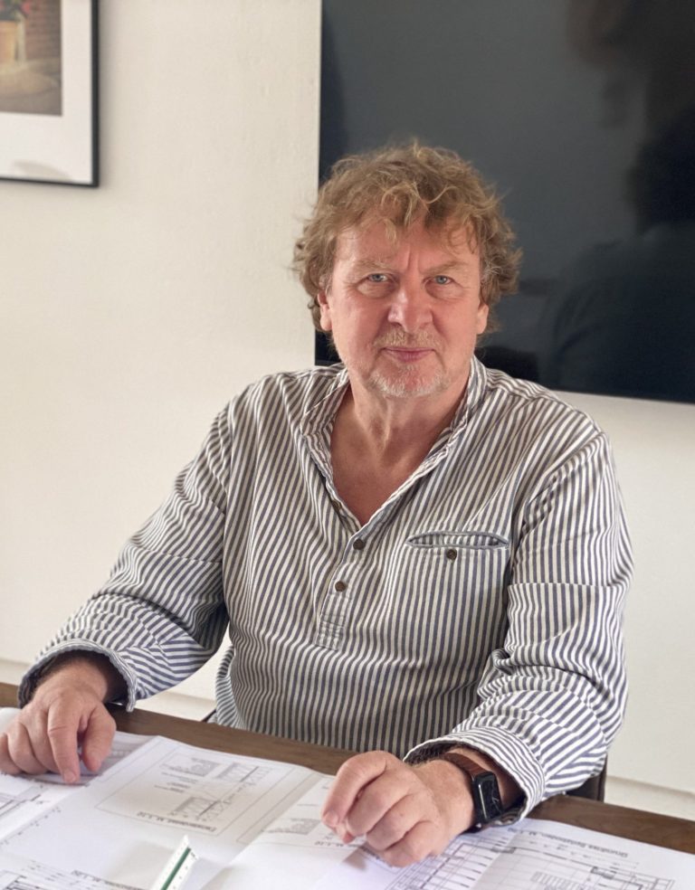 Ingolf Christianus Mann mit lockigem Haar sitzt am Tisch und schaut in die Kamera.